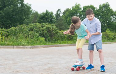Parkta, temiz havada, çocuk taş bloklar üzerinde bir kaykay binmek için kız öğretir