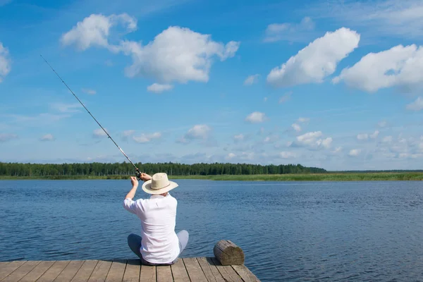 Homem Chapéu Sentado Cais Lança Uma Vara Pesca Contra Céu — Fotografia de Stock