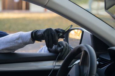 siyah bir eldiven içinde hırsızın eli, açık cam ile, arabanın önünden akıllı telefon alır, tel kırma