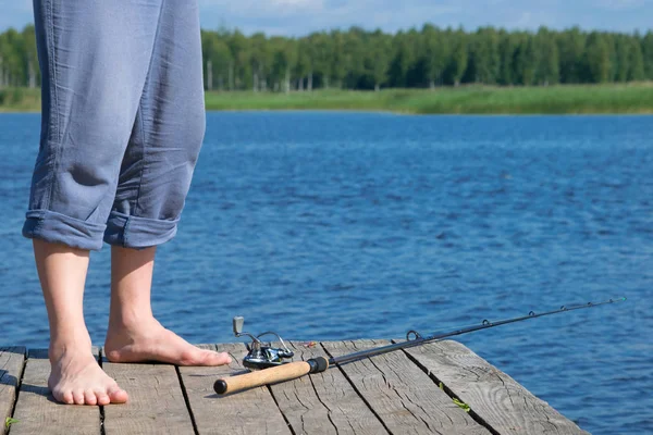 釣り竿の近くの桟橋の漁師の足は 湖の背景に横たわっています — ストック写真