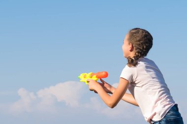 mavi bulutlu gökyüzüne karşı bir su tabancası ile oynayan kız