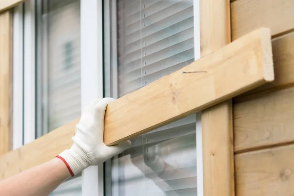 gloved hand holds a board in front of a window to protect windows from natural disasters