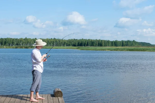 帽子をかぶった男が天気の良い日に湖で休暇中に釣りをしている — ストック写真