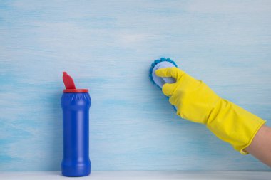 açık mavi bir arka plan, sarı kauçuk eldiven bir el, yüzey fırçalar, yanında temizlik tozu ile açık bir mavi şişe