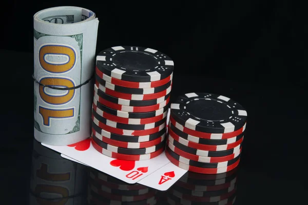 two stacks of colored chips, for playing in the casino, next to a roll of dollars, on a black background with cards