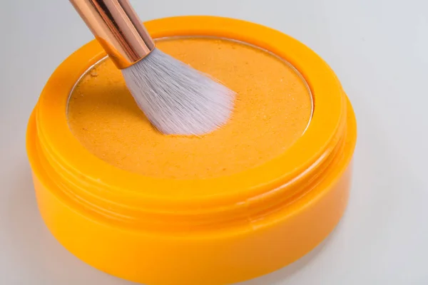 close-up of orange powder in a box for application to the hair, with a brush on a white background