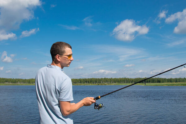 a man in yellow glasses, against a beautiful landscape, throws a fishing rod into the lake to catch fish