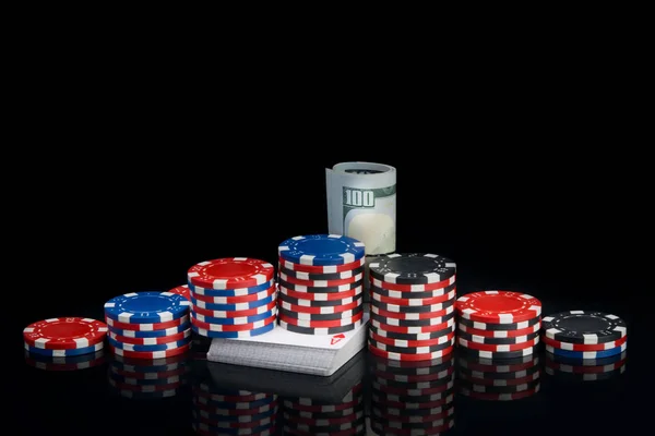 反射のある黒い背景に カードのデッキに ポーカーをプレイするためのロールに包まれた色のチップとドル紙幣のピラミッドがあります — ストック写真