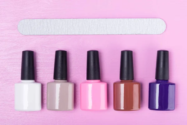 Concept for nail service: colorful nail polishes and nail file on a pink background