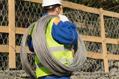 Tulumlu işçi omuzlarında bir bobin taşıyor, dikiz aynasından.