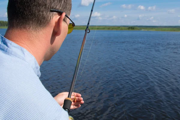 close-up, a man holding a fishing rod and a hook for fishing, against the lake