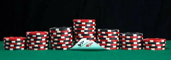 緑色のテーブルの上に ポーカーをプレイするために 異なる色のチップのピラミッドと2つの上げられたカード エース 碑文のための黒い背景の上に — ストック写真