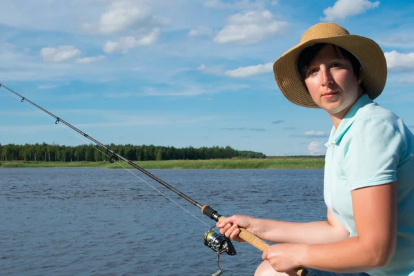 クローズアップ 帽子をかぶった女性は 湖の背景に対して 魚を捕まえるために釣り竿を保持しています — ストック写真