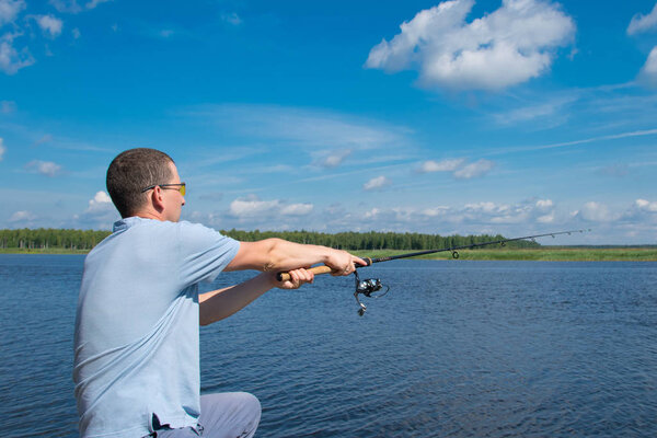 a man in yellow glasses, throws a fishing rod in the lake,for fishing, on the background of a beautiful landscape