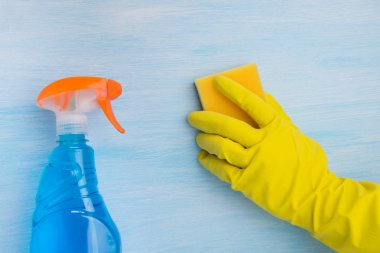 mavi bir arka plan üzerinde, sarı eldiven bir el bir sünger ile yüzeyi temizler, temizlik sıvı bir sprey ile bir şişe yanında