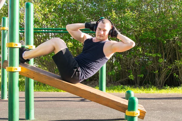 a man plays sports in the open air, listens to music, on a special platform, does an exercise on a press and looks into the camera