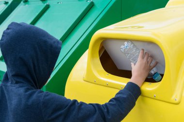 kaputta bir çocuk plastik atık için tasarlanmış sarı bir kap ta boş bir şişe atar