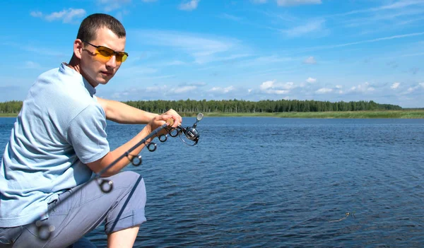クローズアップ 黄色い眼鏡をかけた男 桟橋に座って 美しい風景に対して 魚をキャッチするために湖で回転を投げる — ストック写真