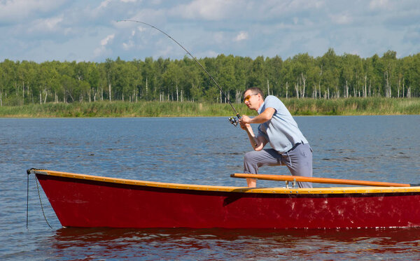 a man in a boat, in the center of the lake, throw a fishing rod to catch a big fish, against the backdrop of a beautiful landscape
