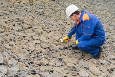 mavi üniforma lı ve beyaz kasklı işçi, zemin taşları için bir ızgarayı onarıyor
