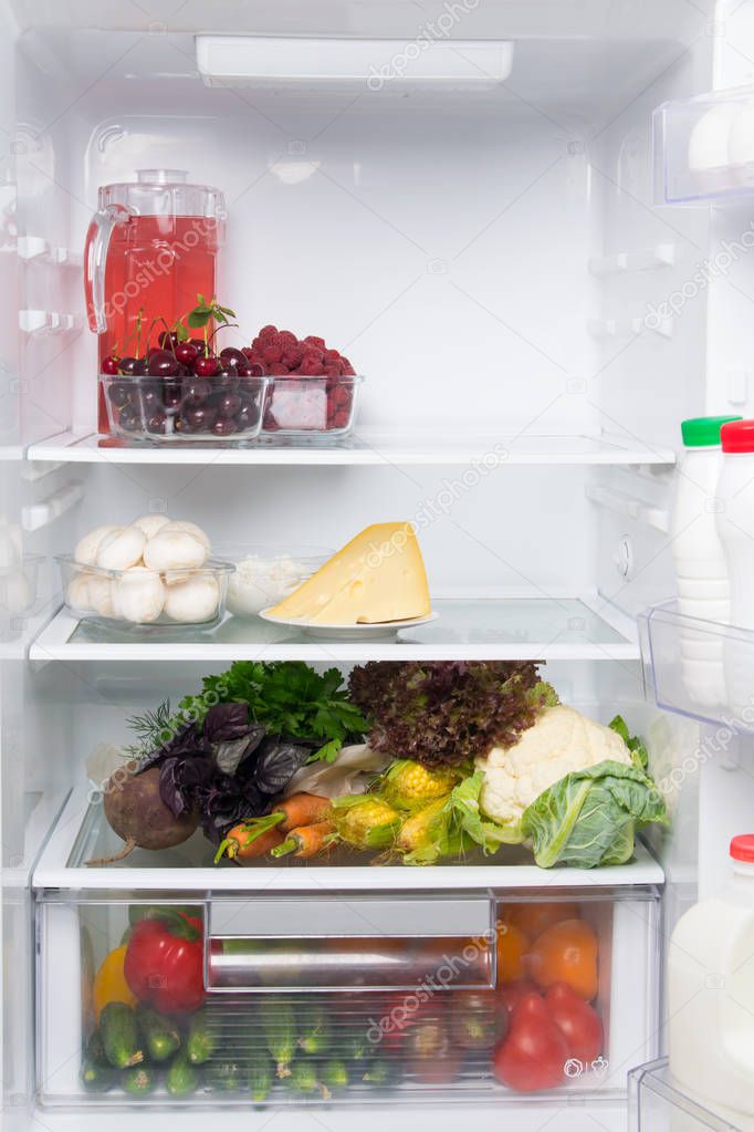 on the shelves of a white refrigerator, food stock, fresh vegetables, berries, cheese, mushrooms, cottage cheese, compote in a jug, and in the door dairy products, kefir, cream
