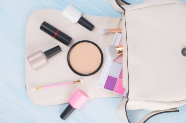 hafif bir arka plan üzerinde, beyaz bir kozmetik çantası, manikür ve makyaj için dağınık öğeler, renkli göz farı, fırçalar, yüz tozu, oje ve kırmızı lipstic