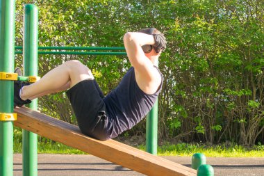 bir adam spor için açık havada gider, müzik dinler, özel bir platformda ve bir basın üzerinde bir egzersiz yapar
