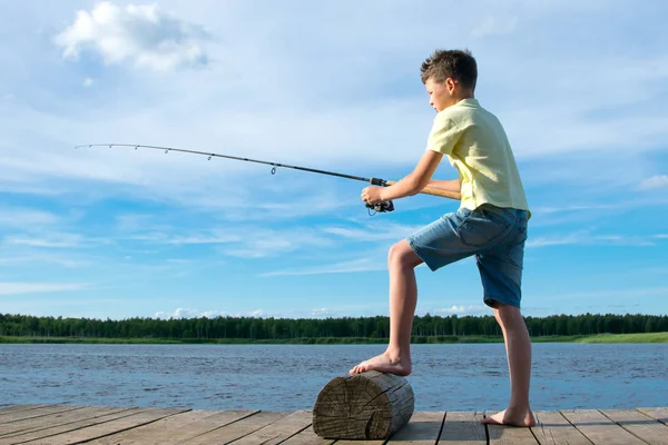 桟橋の少年は 青い空と湖を背景に 餌の上に魚をキャッチ — ストック写真