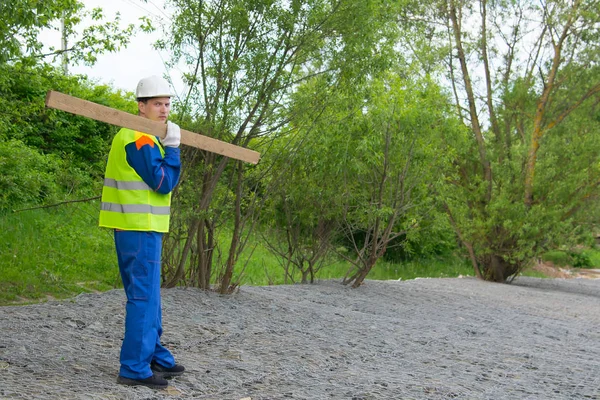 Builder Blue Uniform White Helmet Carries Wooden Beam Stone Embankment — Stock Photo, Image