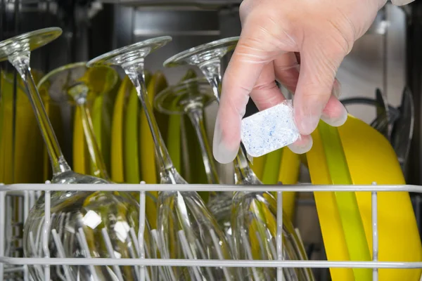 hand in a protective glove, puts the cleaning capsule in the dishwasher after loading items close-up
