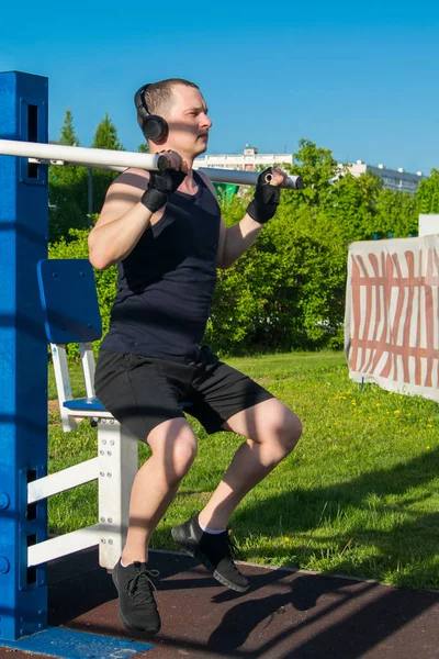man exercising on a street simulator, to strengthen the back, listening to music