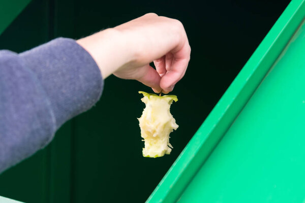 рука бросает кусок яблока в мусорный бак, крупным планом
