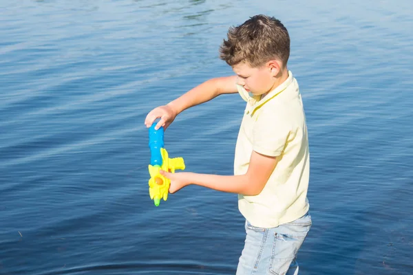 遊ぶ湖を背景にピストルに水を引く少年のクローズアップ — ストック写真
