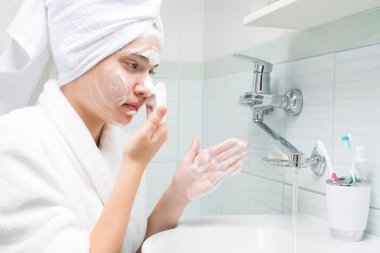 bornozkız bir ayna önünde duruyor, banyo akne ve siyah nokta yüzünü yıkar, yandan görünümü