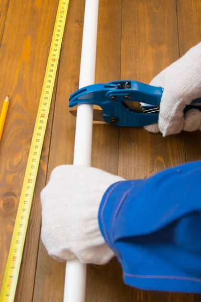 koyu ahşap arka plan üzerinde, beyaz eldiven bir işçinin elleri, su kaynağı onarmak için makas ile bir polipropilen boru kesti