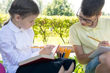 okul üniformalı bir erkek ve bir kız sıcak bir sonbahar gününde yolda bir parkta otururken ödevlerini yapmak