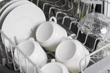 bulaşık makinesinin kafesinde kahve ve tabaklar için dört temiz beyaz fincan, yakın çekim görünümü