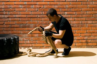 bir tuğla duvara karşı, siyah üniformalı bir adam, bir ip ve lastik ile çapraz-fit yapan, yakın çekim