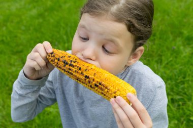 kız yeşil çim karşı, iştah ile ellerini mısır ve ısırıkları bir kulak tutar.