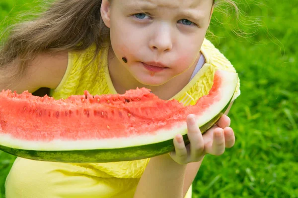 girl eating sweet watermelon, stained face. against the green lawn
