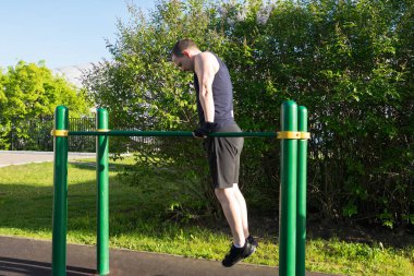 bir adam sokakta bir spor alanında iki bar üzerinde vücudunu yükseltir