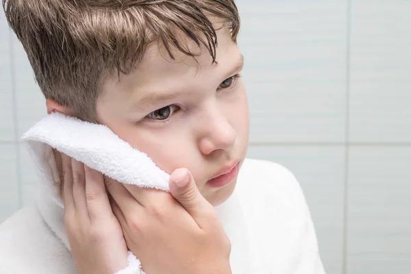 boy wipes his face with a white towel, front view close-up