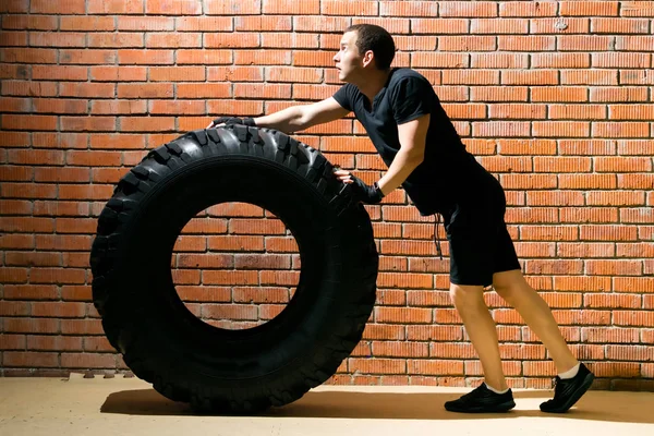 bir tuğla duvara karşı, siyah spor üniformalı bir adam, bir lastik lastik ile spor yapan