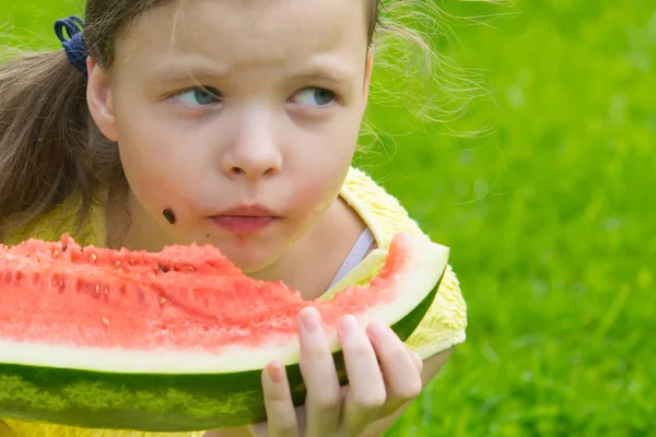 girl eating sweet watermelon, stained face. on the background of the green lawn there is a place for the inscription.