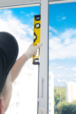 mavi bir başlık bir işçi, sarı bir seviye yardımıyla, gökyüzüne karşı, plastik bir pencerenin çerçevedoğru kurulum kontrol