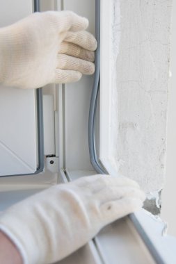 koruyucu bir eldiven içinde ustanın elleri, plastik bir pencere nin çerçevesine ekler, sızdırmazlık için elastik bir bant, yakın çekim