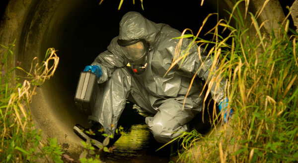 scientist in protective clothing, with a suitcase comes into the drain pipe, to take samples, close-up