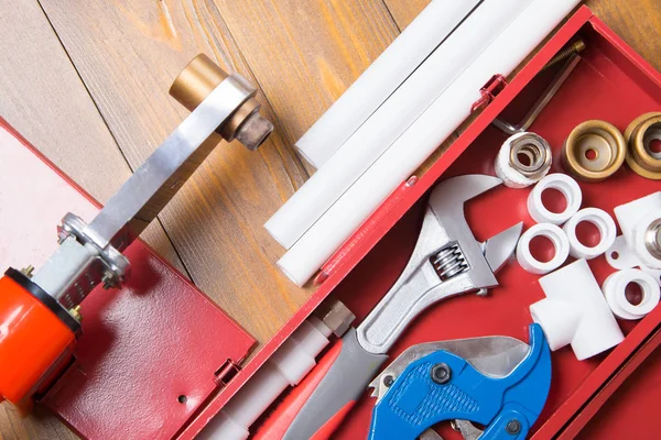 polypropylene pipes and soldering tool, in a red box, on a dark wooden background and blue scissors with key, close-up