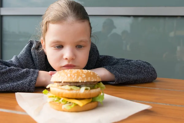 Menina Adolescente Olhando Apetitoso Burger Deitado Frente Dela Mesa — Fotografia de Stock