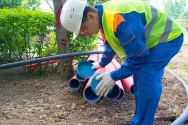 Koruyucu üniformalı işçiler, plastik borulara su geçirmemek için bir kapak yerleştirirler.
